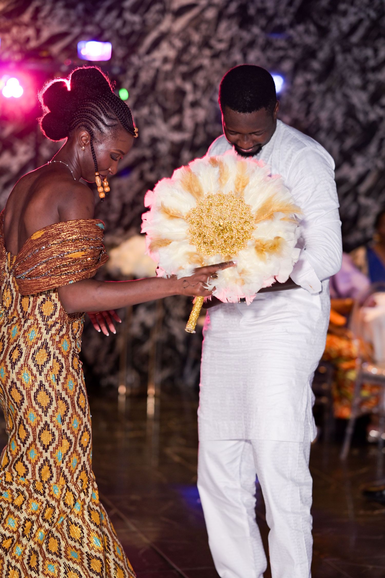 Dancers moving energetically, one in white attire and another in a patterned dress with a fan.