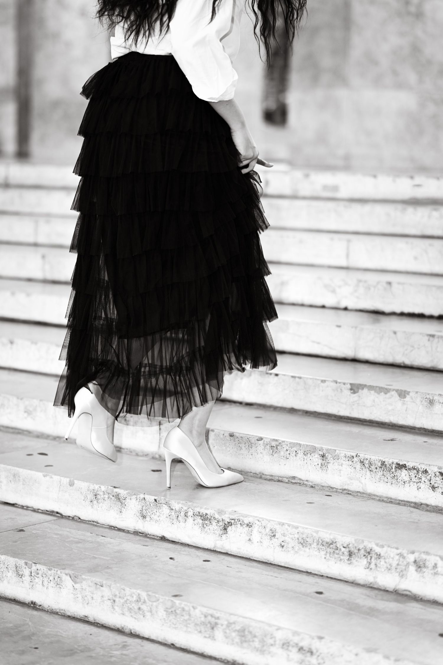 Black and white photo of layered tulle skirt and heels on concrete steps.