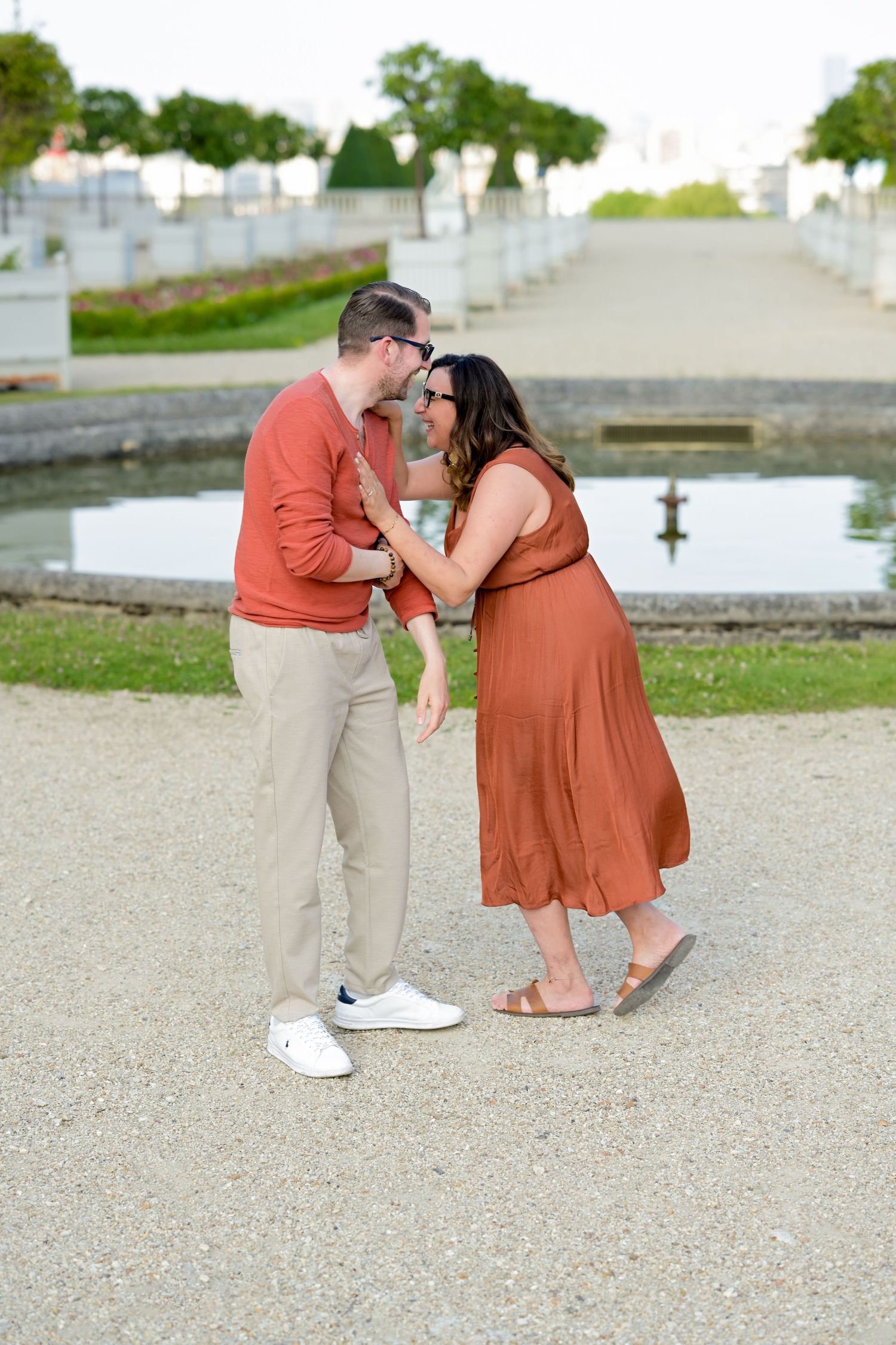 A couple in coordinating rust and khaki outfits shares playful moments on a gravel path.