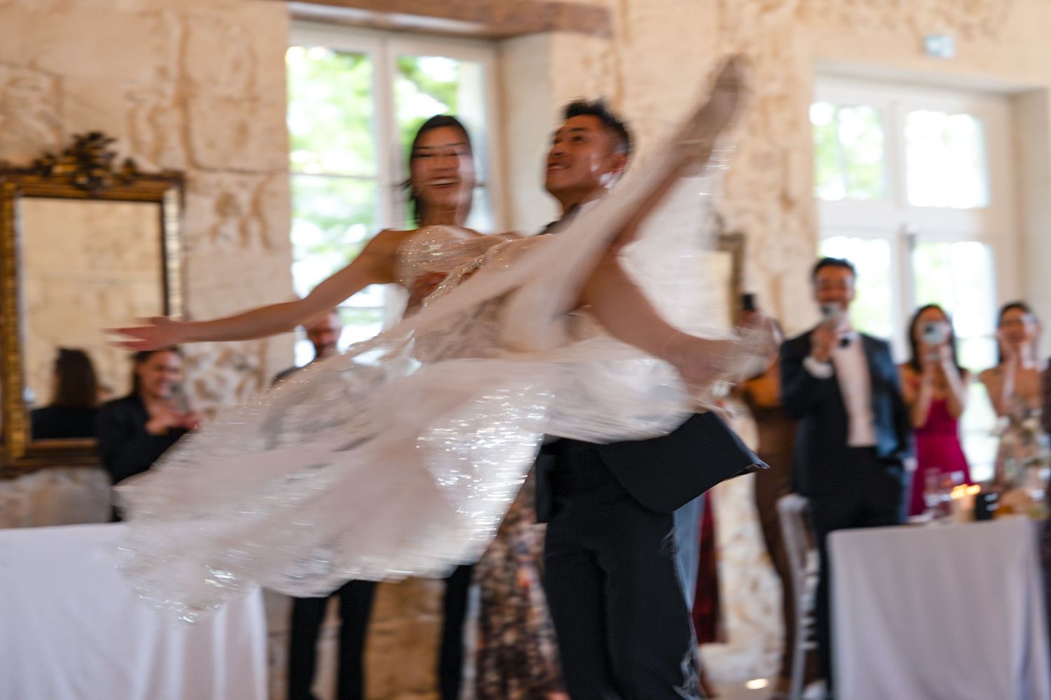 A couple performs a dramatic dance move during their wedding reception in a stone-walled venue.