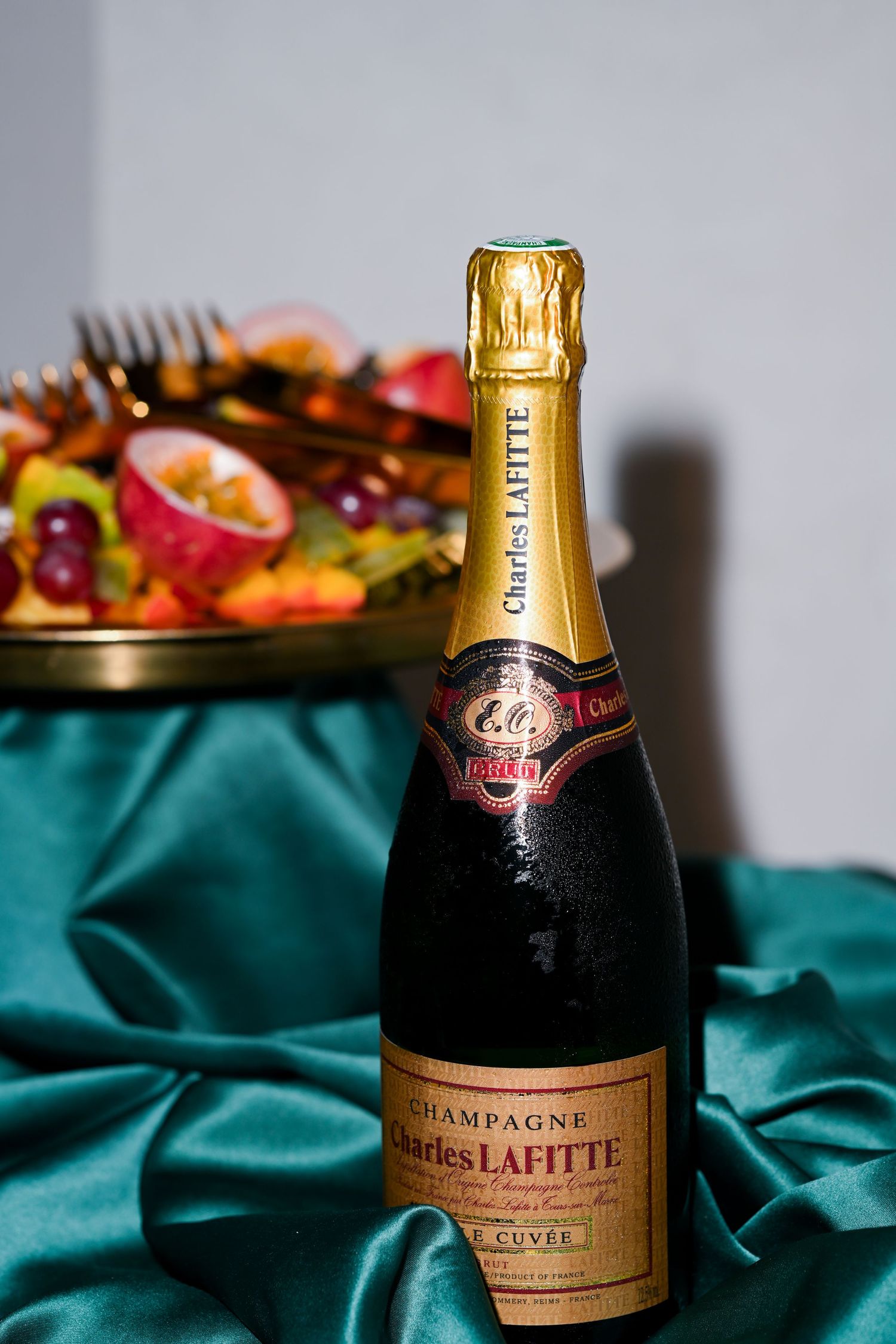 A bottle of Champagne Lafitte sits on a teal cloth next to a platter of appetizers.