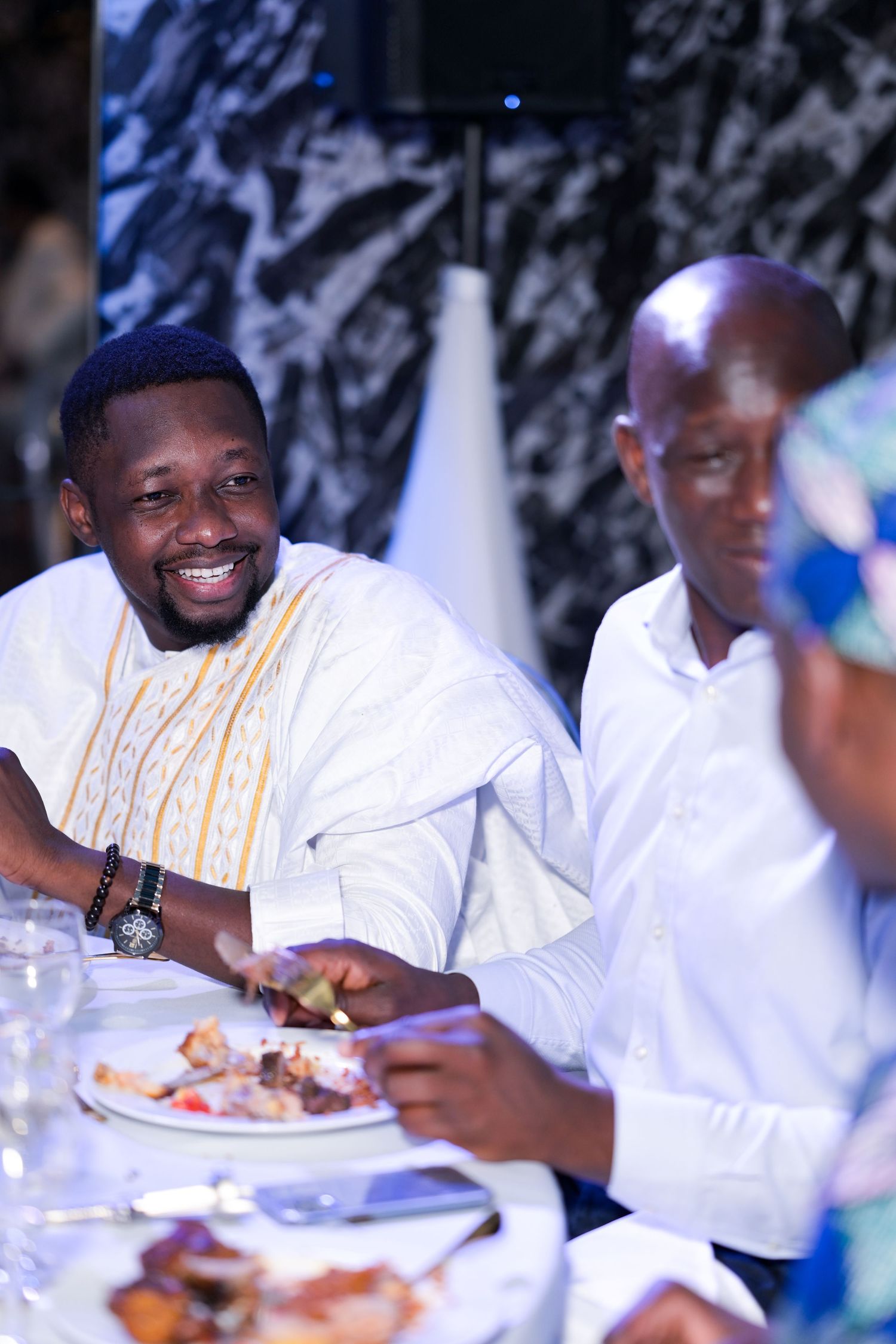 Guests in white attire enjoying a formal dinner celebration.