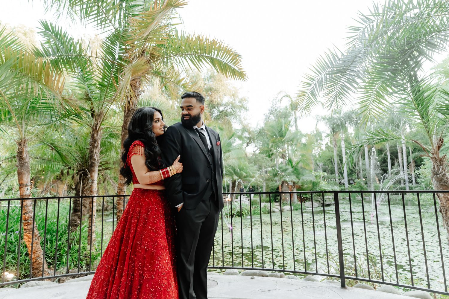 Couple poses in formal attire against a tropical palm garden backdrop.