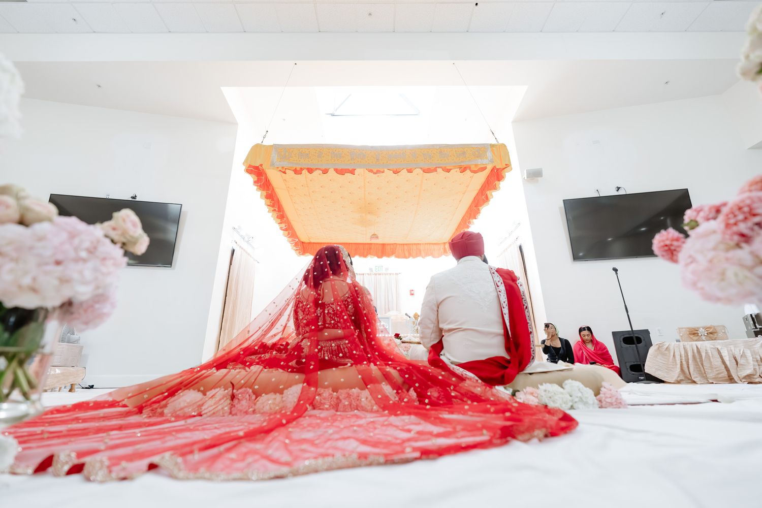 A stunning red bridal lehenga with intricate embroidery spreads across a white bed during wedding preparations.