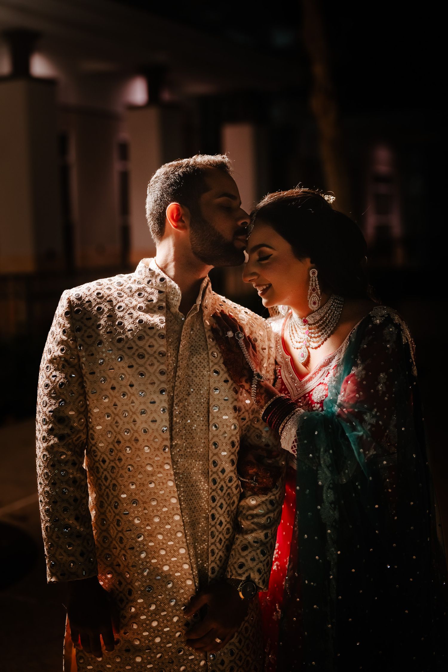 Intimate low-light portrait of a couple in sparkly traditional South Asian wedding attire.