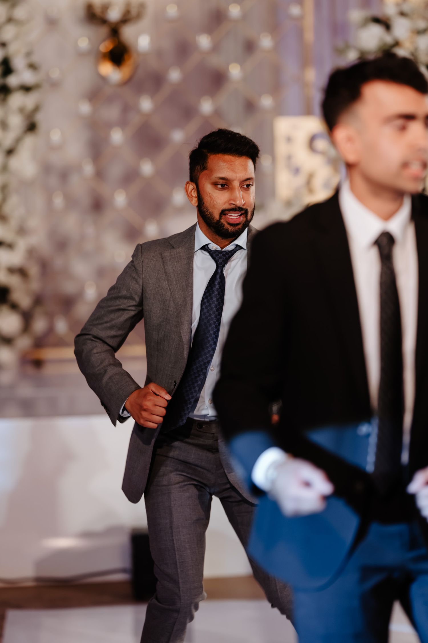 Two men in formal suits dancing and celebrating at an elegant indoor event.