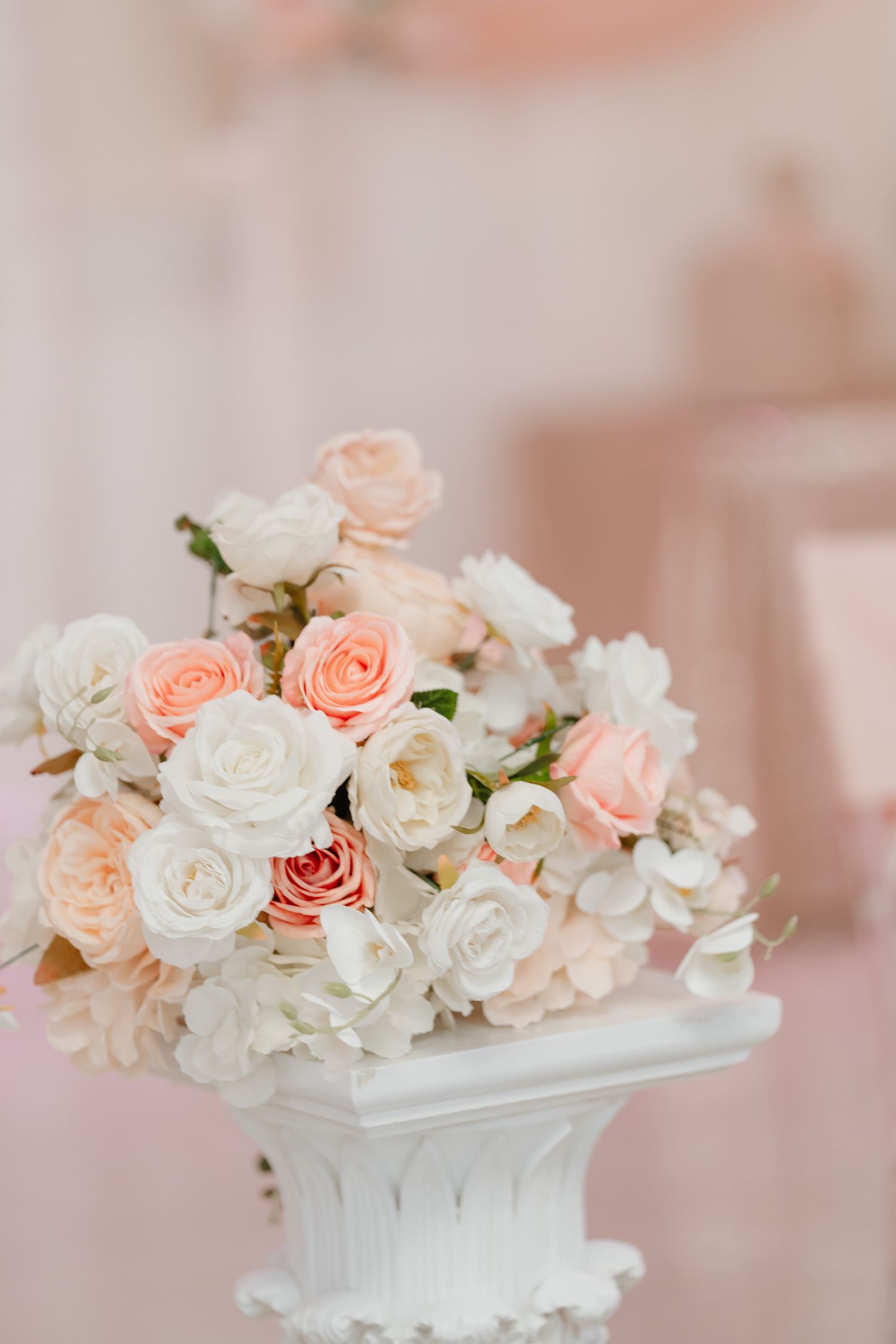 Delicate arrangement of white and peach roses in a vintage white ceramic container against soft pink background.