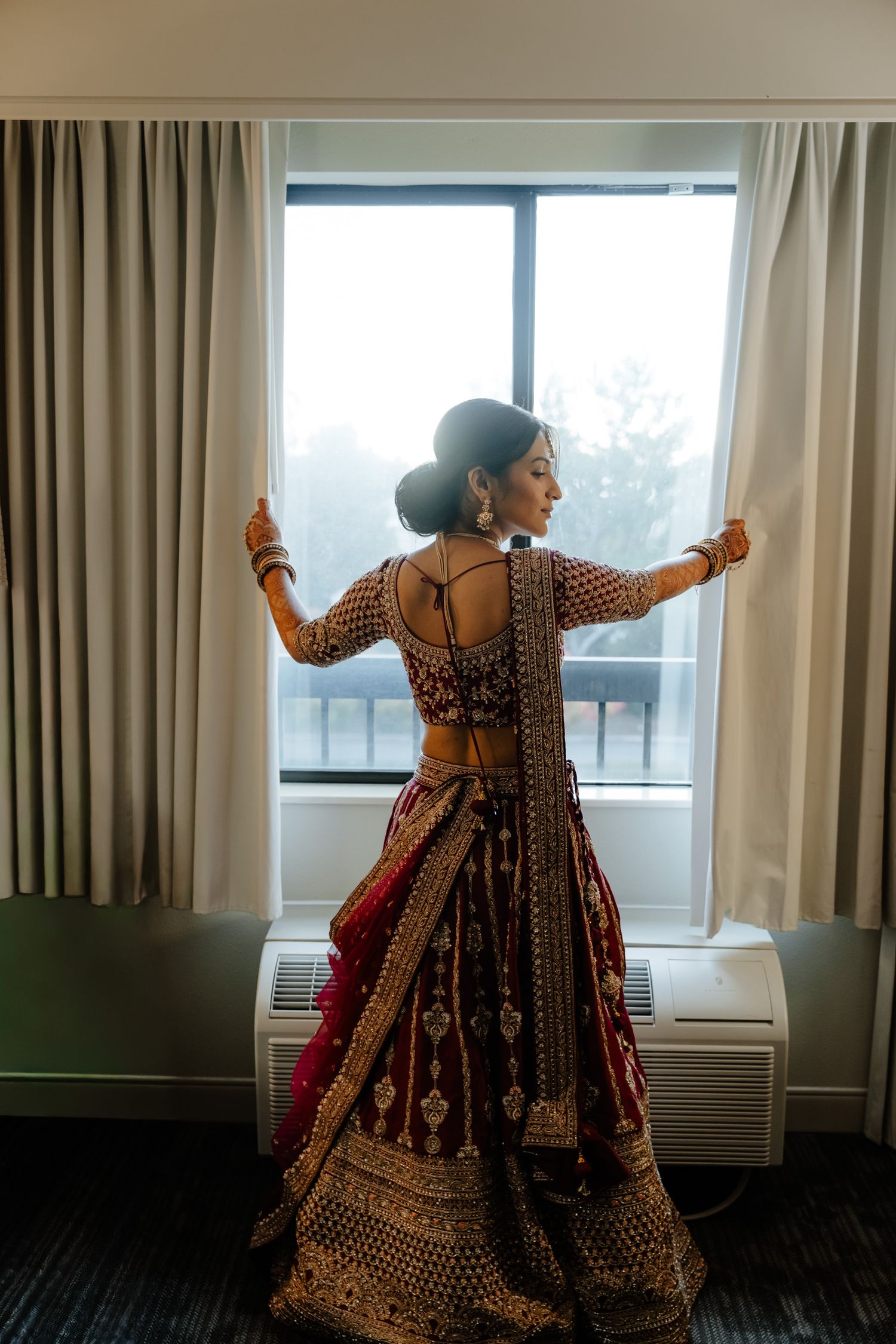 Traditional Indian bridal dress being showcased in a hotel room with window views and natural lighting.