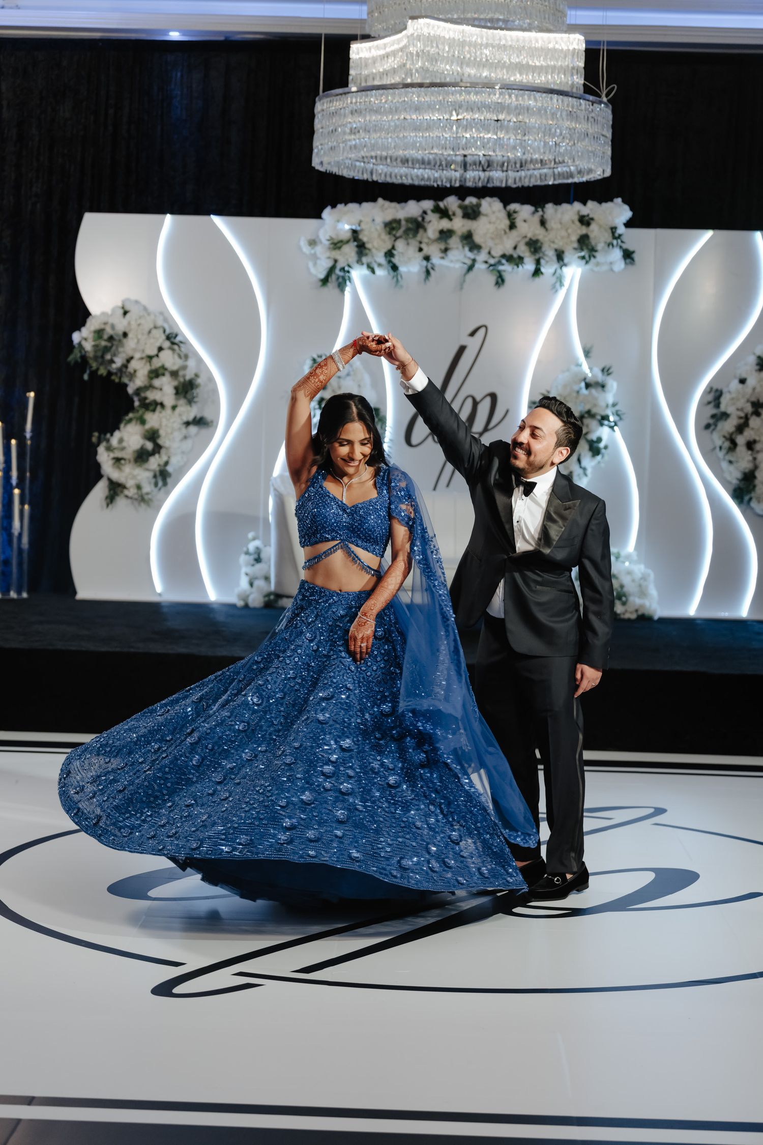 A couple dances elegantly on a white circular floor as the bride's flowing blue gown sweeps dramatically around them.