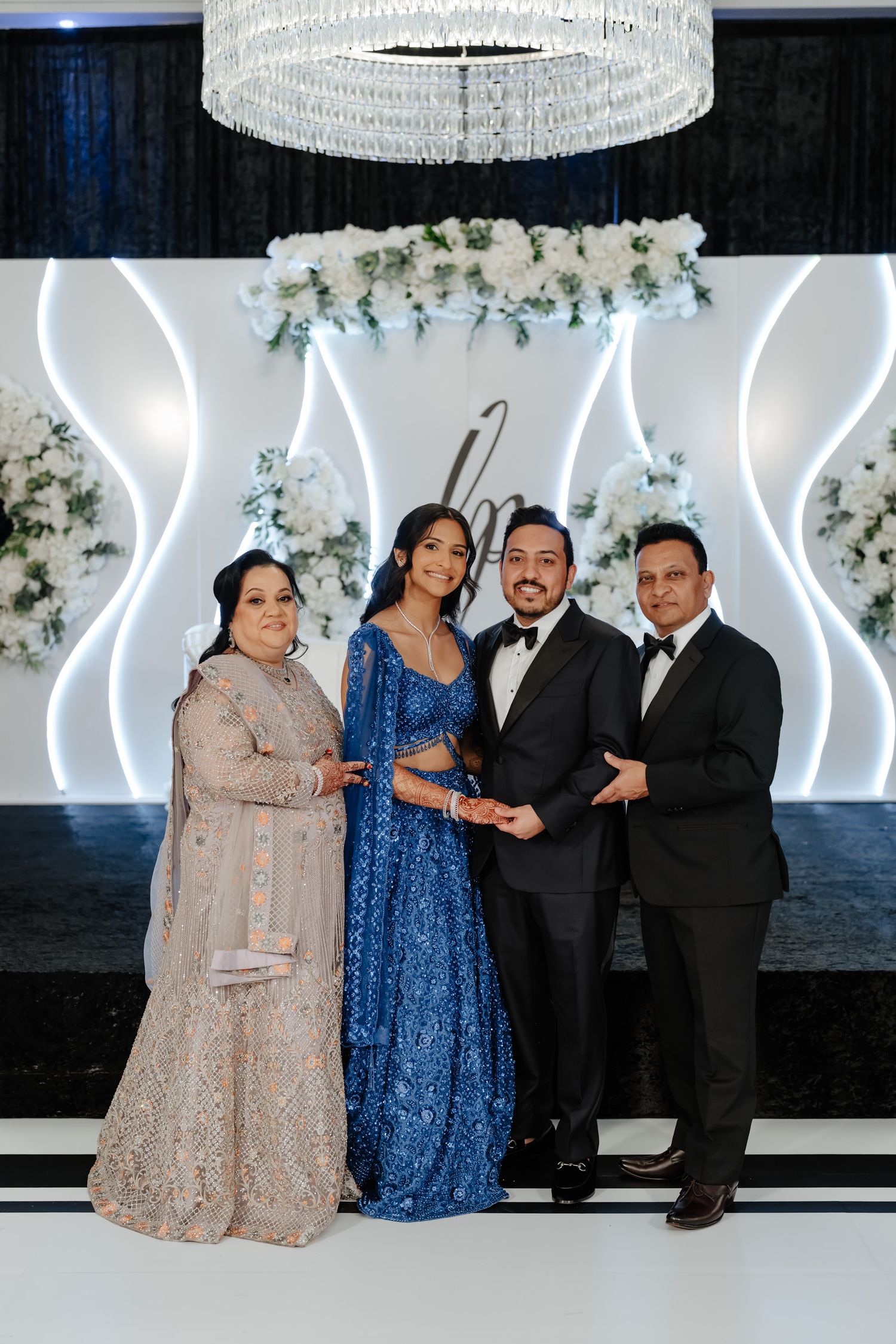 Group photo at an event with people wearing formal attire including blue and beige dresses against a white backdrop.