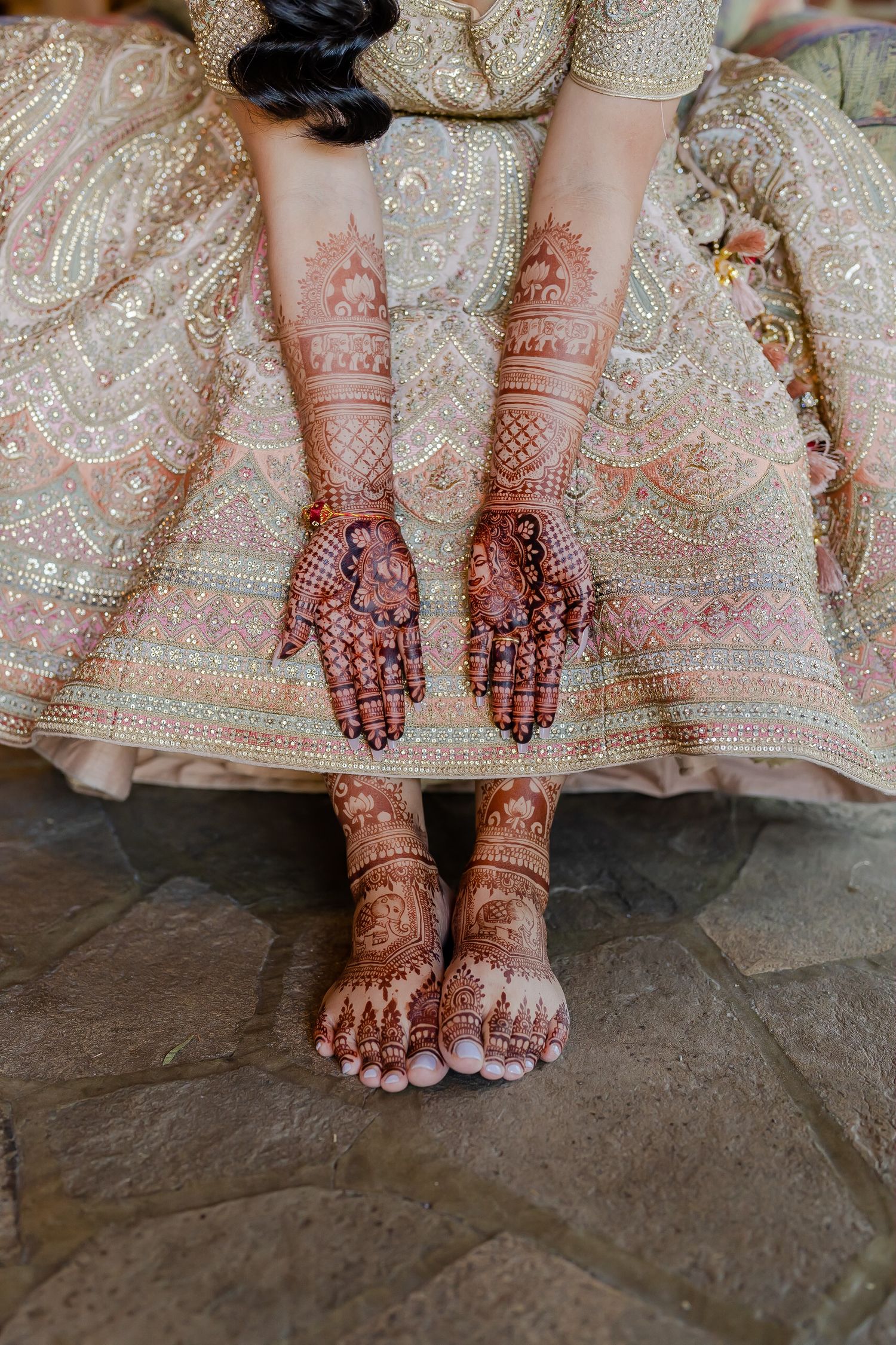 Close-up view of intricate henna designs on hands and feet with traditional Indian bridal attire and jewelry.