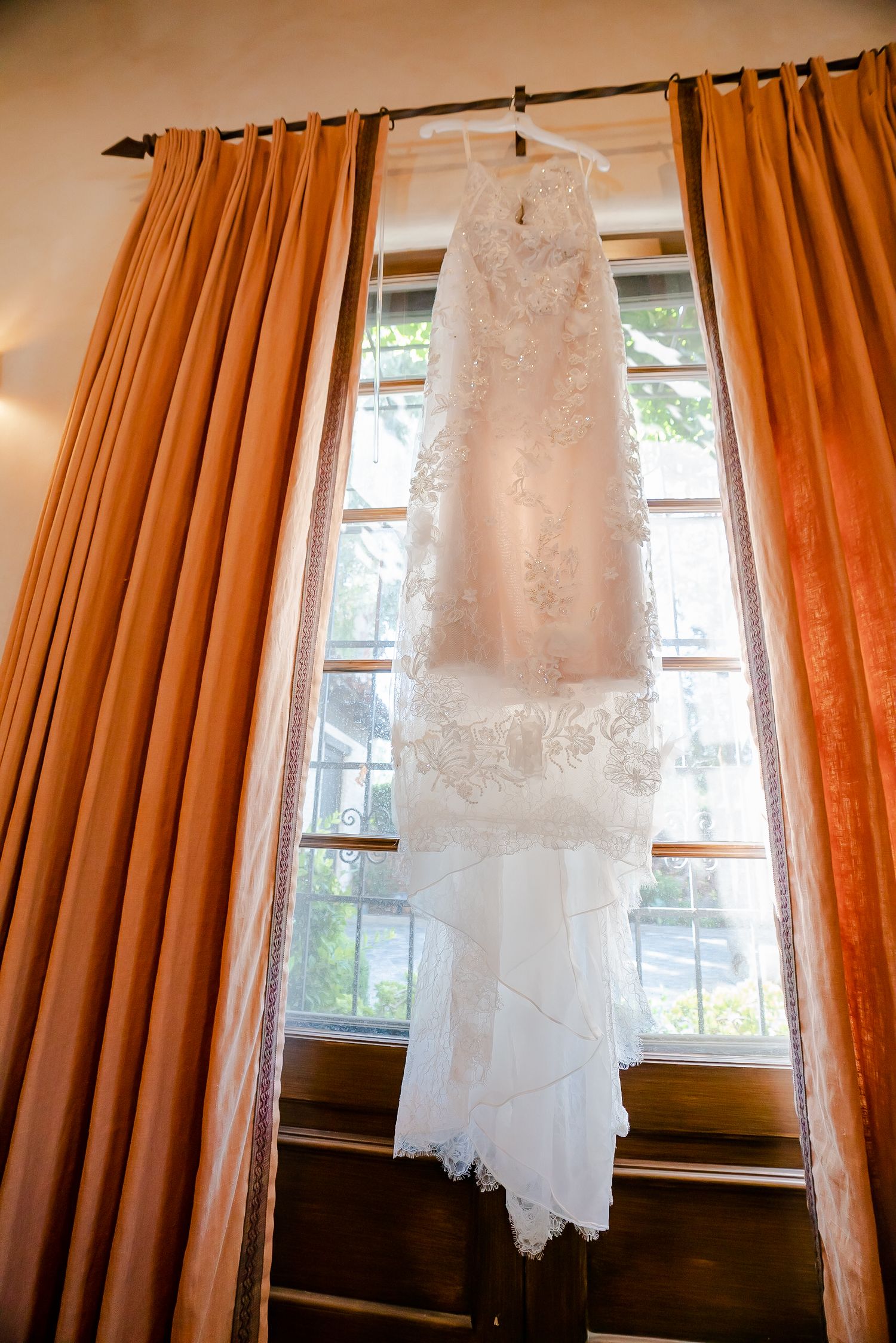 A white lace wedding dress hangs in front of a window with orange curtains in a sequence of similar shots.