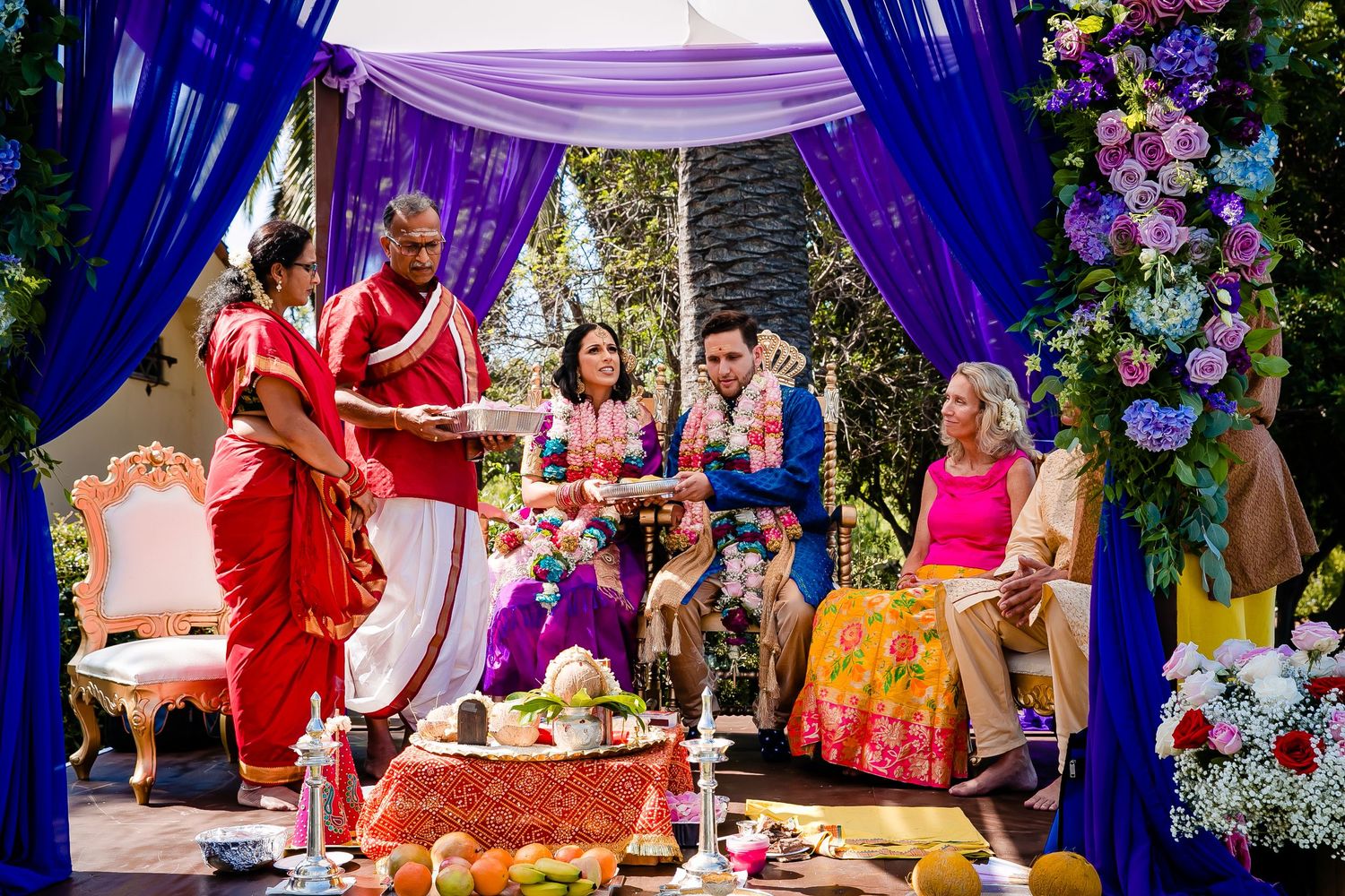 Traditional Indian wedding ceremony with purple and red decorations featuring cultural rituals under an ornate mandap.