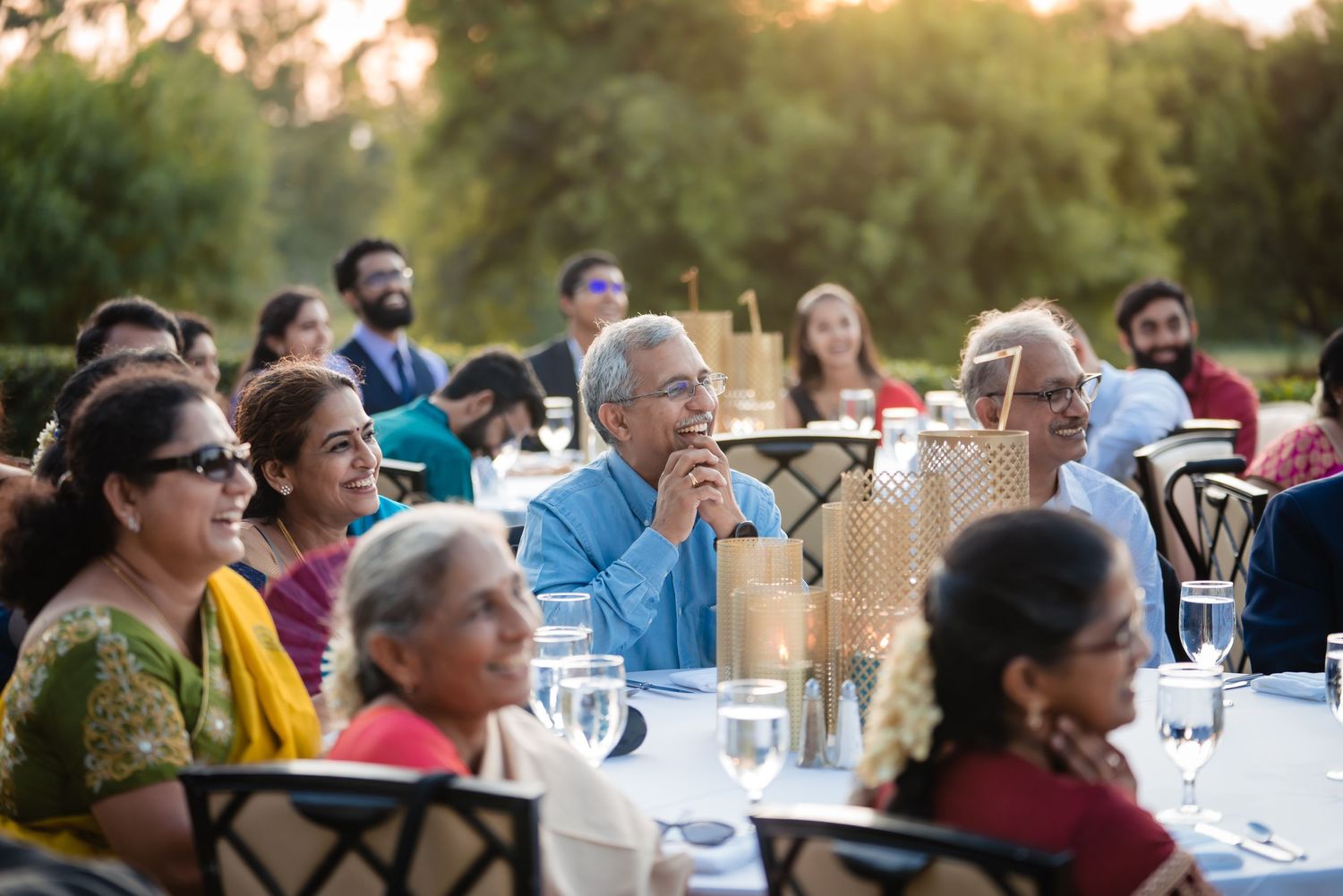 People seated at outdoor tables during a sunset gathering with warm lighting and natural surroundings.