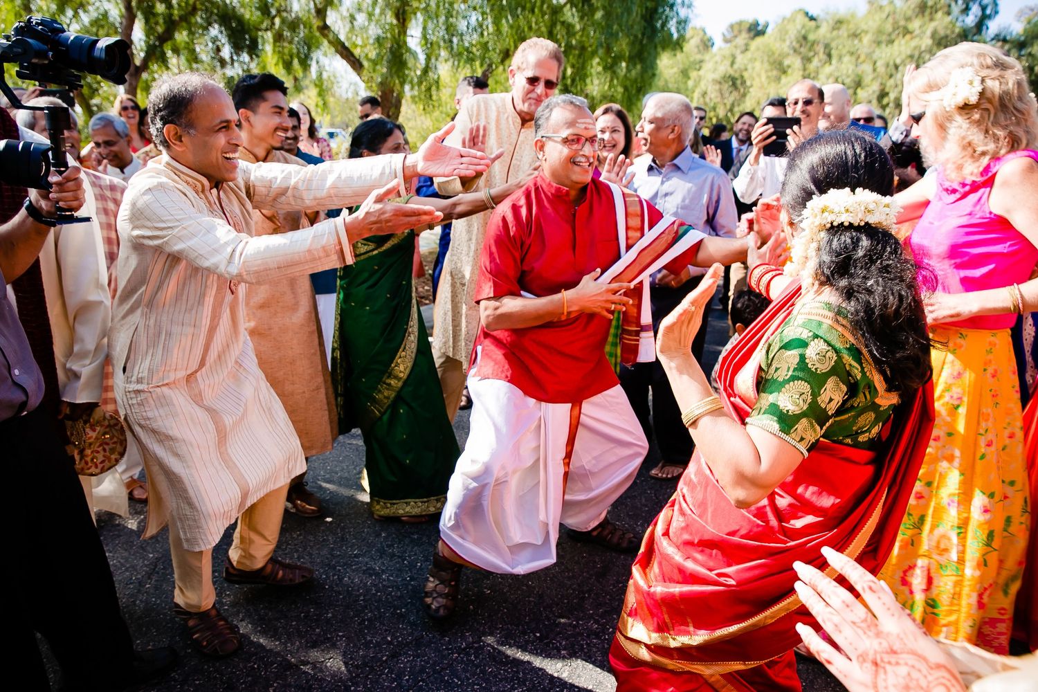 People dance and celebrate at an outdoor wedding reception with colorful traditional outfits and decorations.