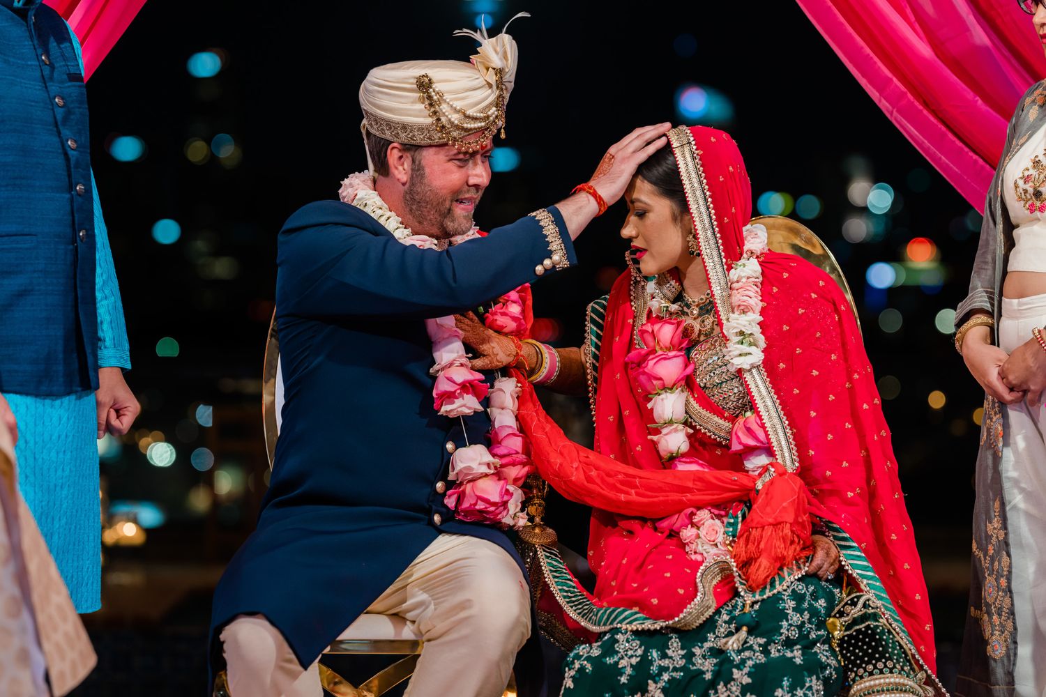 Wedding celebration with bright red and pink decor under evening lighting.