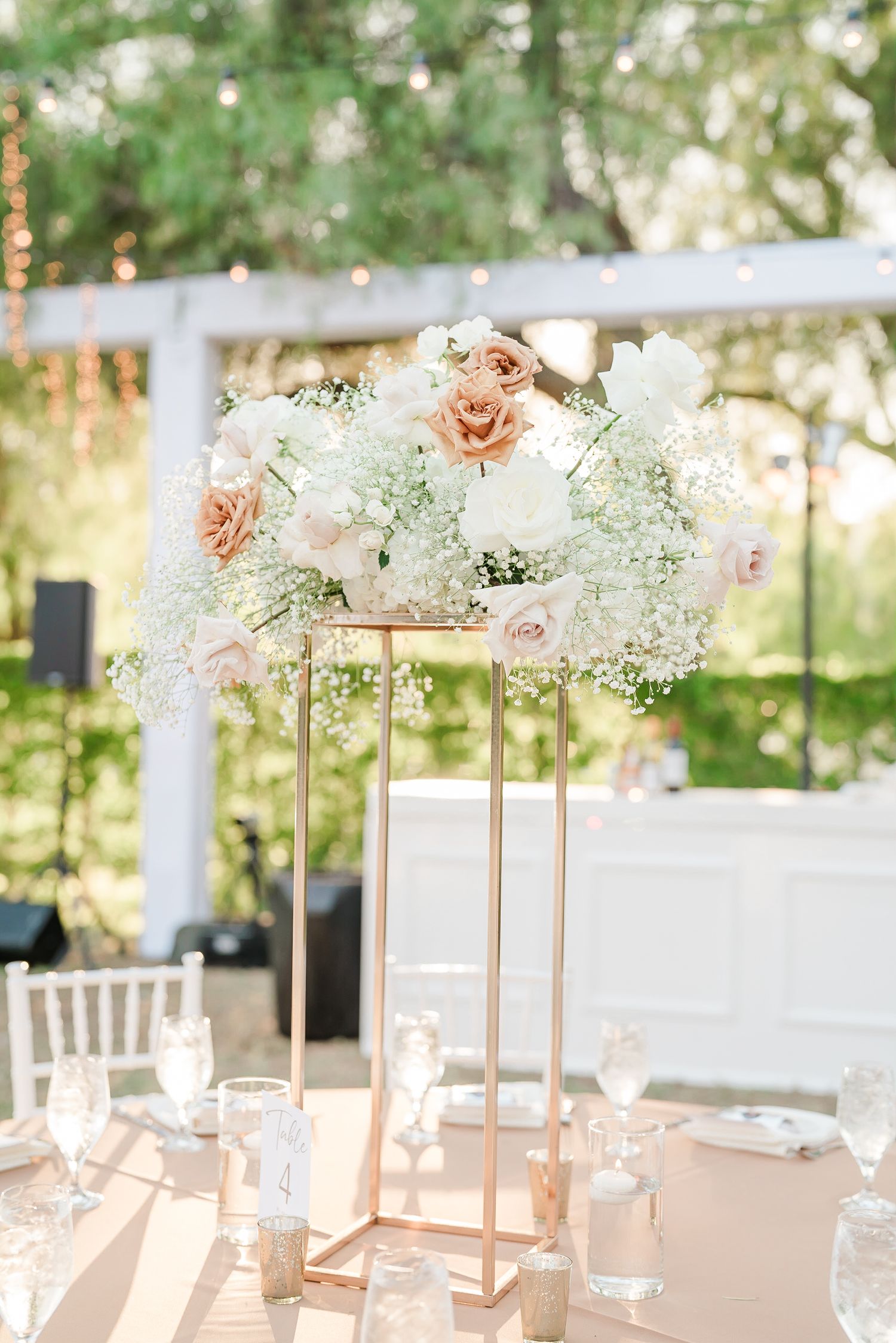 Elegant wedding centerpiece featuring pink roses and baby's breath on a tall gold stand with candles.