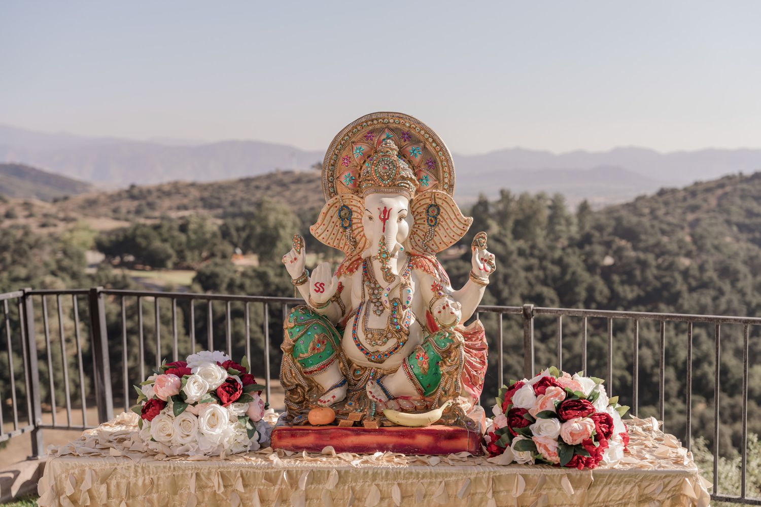 Scenic outdoor wedding ceremony setup with mountain views, floral arrangements, and a decorated mandap structure.