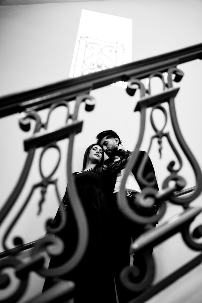 Couple embracing on ornate iron staircase in black and white photo.