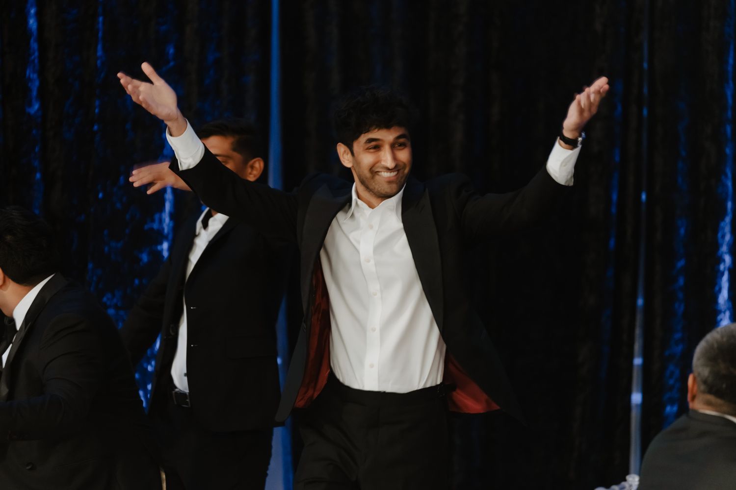 Formal event with people dancing and celebrating against dark backdrop with stage lighting.