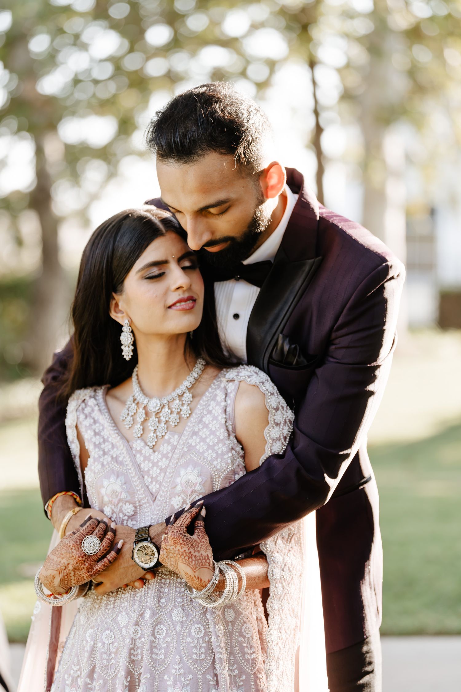 Couple in traditional wedding attire sharing tender moments in a sunlit garden setting.