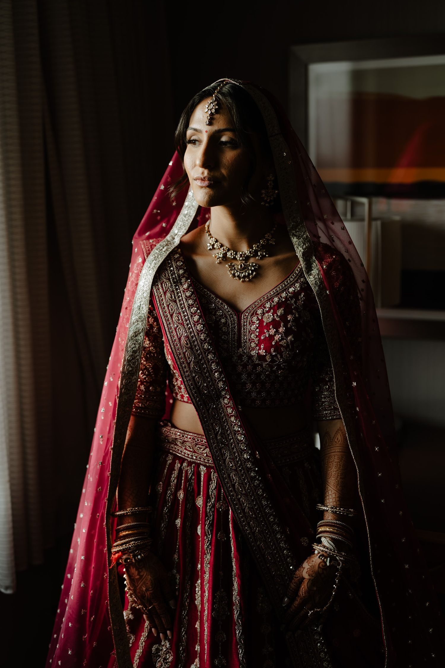 Traditional South Asian bridal attire in deep burgundy with intricate embroidery and embellishments.