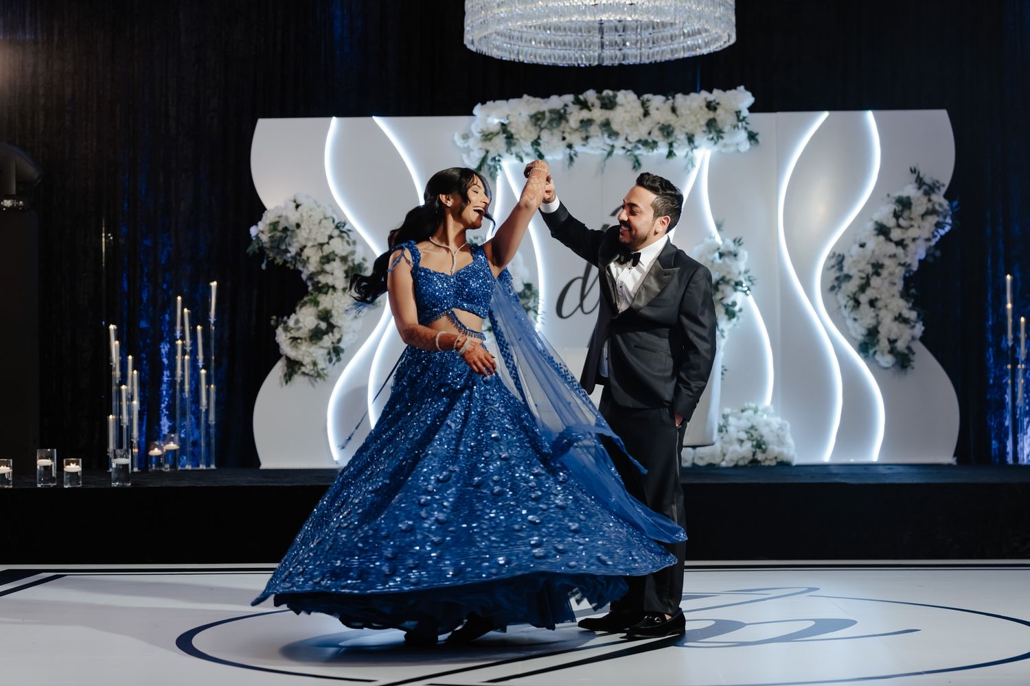 Couple dancing on illuminated floor with sparkling blue gown and elegant decor.