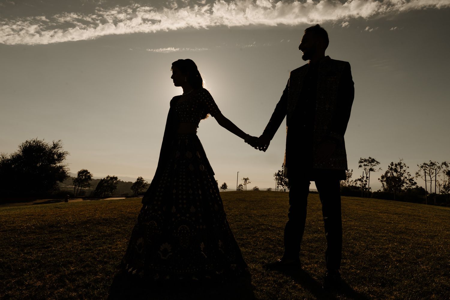 Romantic silhouettes against a sunset sky during an outdoor wedding photoshoot.