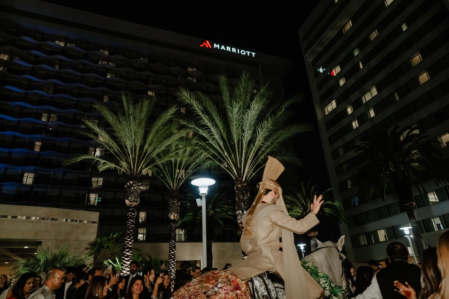 Outdoor evening celebration at a hotel venue with palm trees and string lights creating a magical atmosphere.