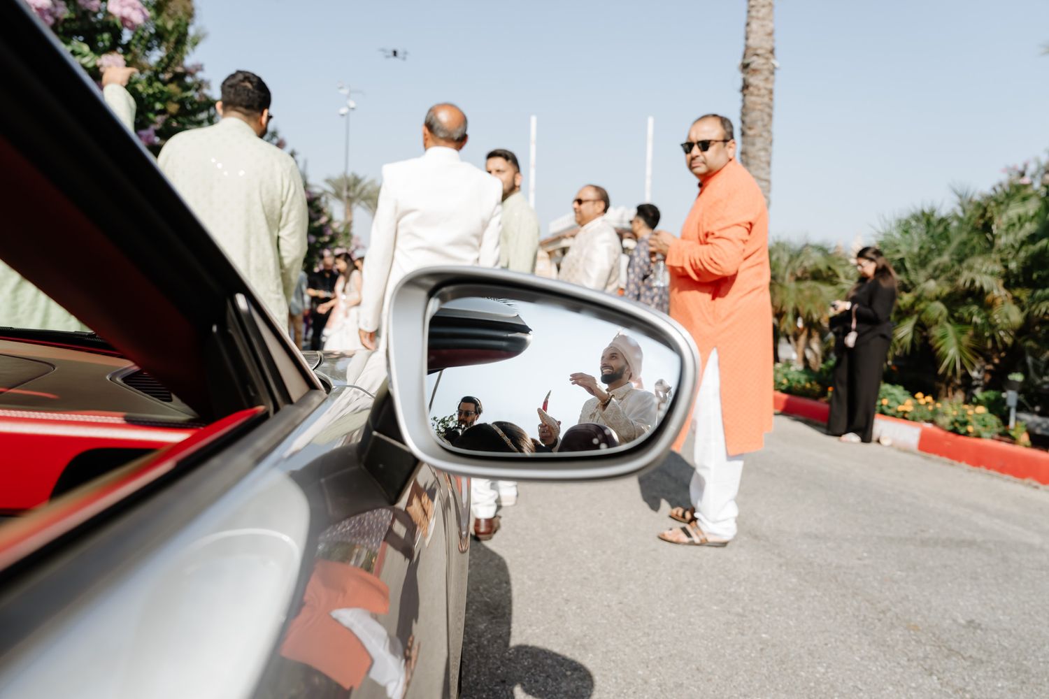 Outdoor celebration with guests in traditional dress gathered near parked cars.
