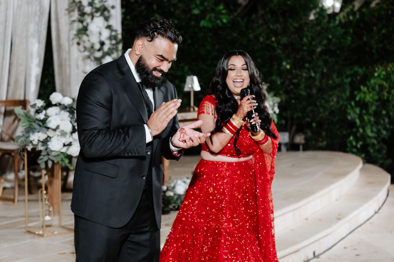 A couple shares joyful moments in formal attire during their wedding celebration against a lush garden backdrop.