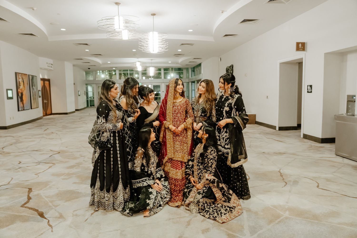 A group wearing ornate traditional South Asian wedding attire poses together in an elegant marble hallway.