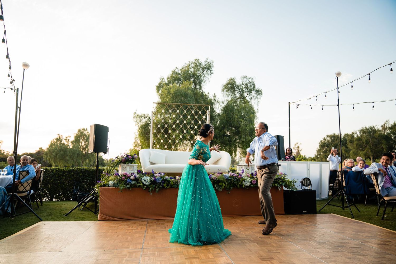 Wedding guests dance and celebrate on an outdoor patio decorated with string lights during a reception.