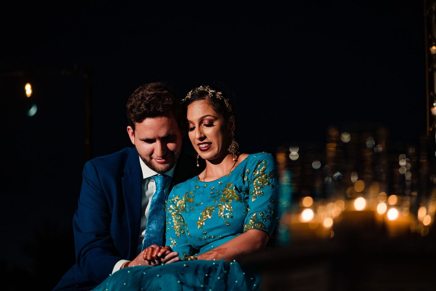 A couple in formal attire share an intimate moment during an evening photoshoot with soft lighting.