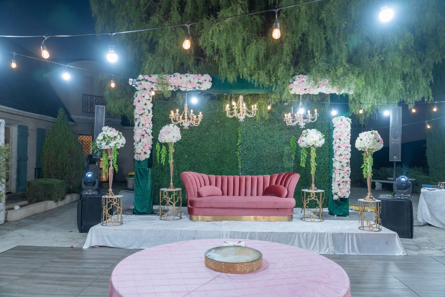 Evening outdoor wedding reception with string lights and elegant decor under willow trees.