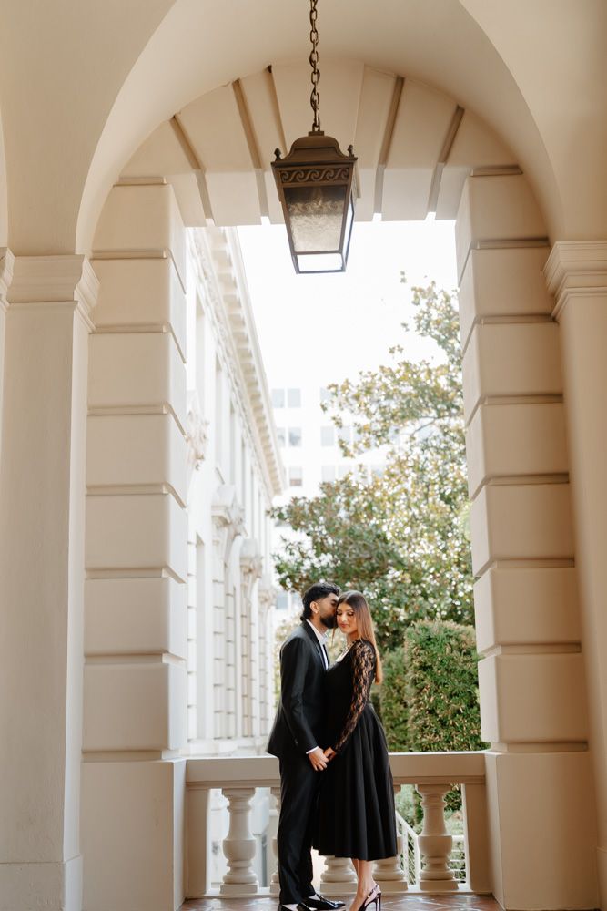 Couple in black attire sharing a romantic moment under an elegant arched colonnade with a vintage lantern overhead.