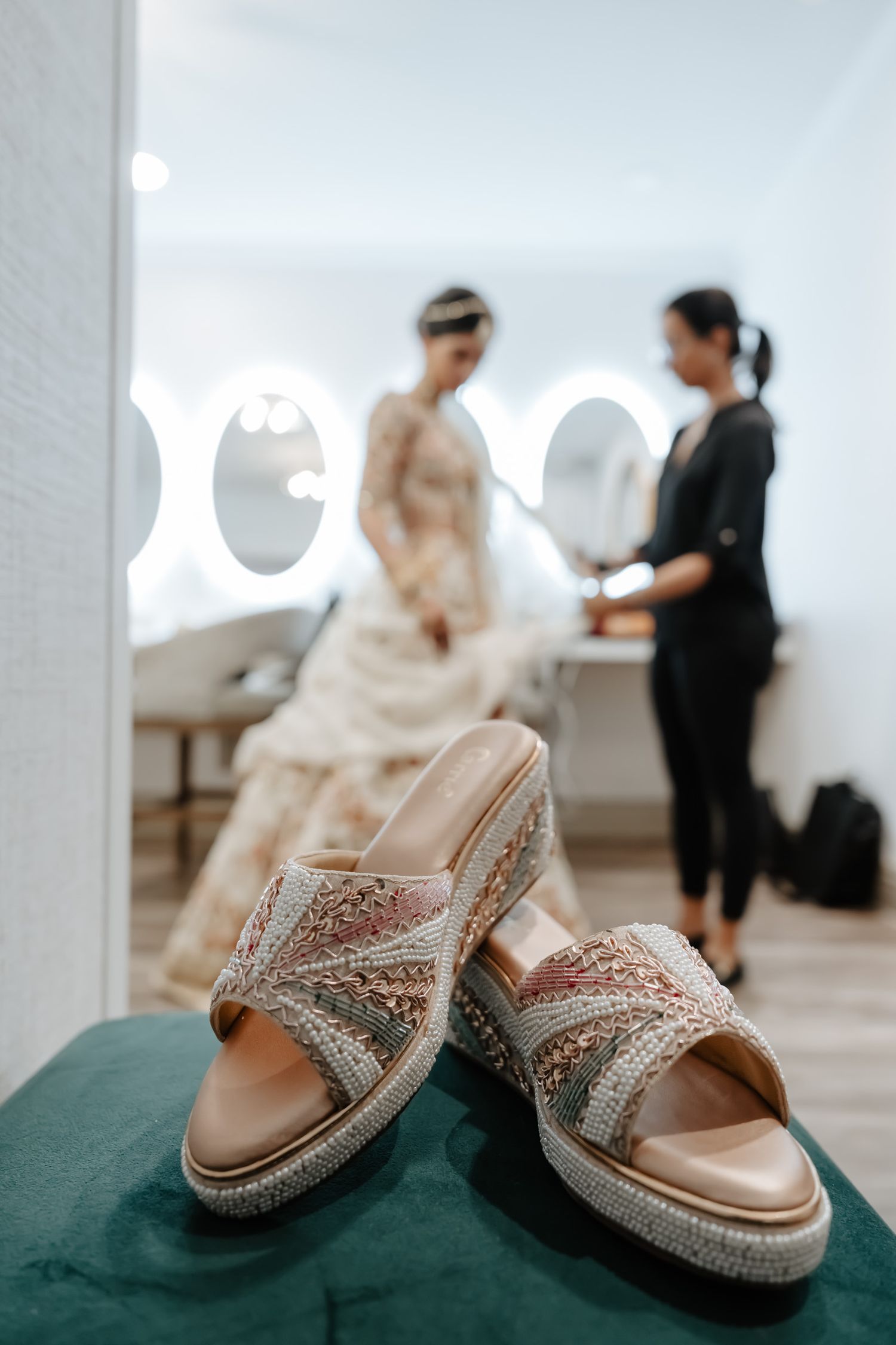 Glittery silver bridal sandals on a teal surface with preparation activities happening in the background.