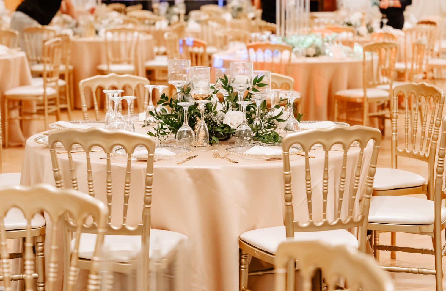 Elegant wedding reception venue with round tables, white chairs, and soft peach lighting creating a romantic atmosphere.