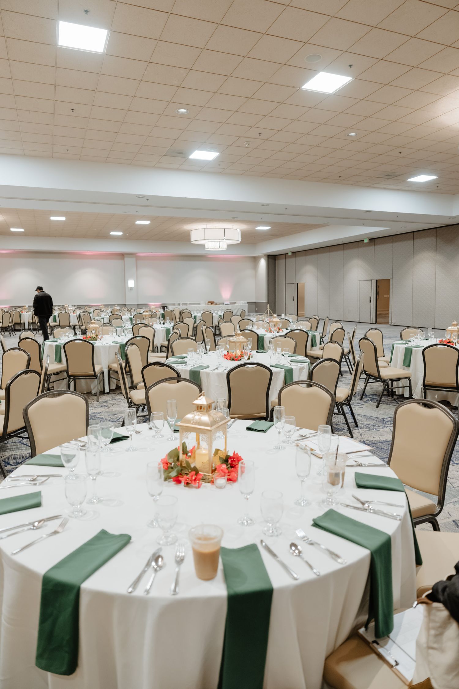A formal banquet hall setup with round tables decorated with white linens and green accents.