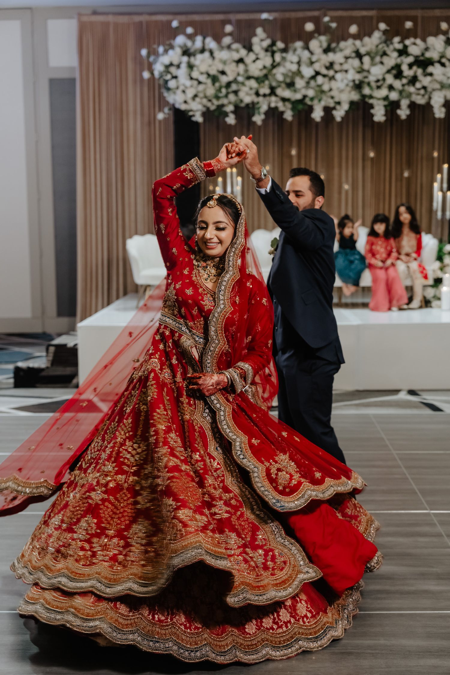 Traditional Indian wedding dance featuring a bride in an ornate red and gold lehenga twirling during a celebration.