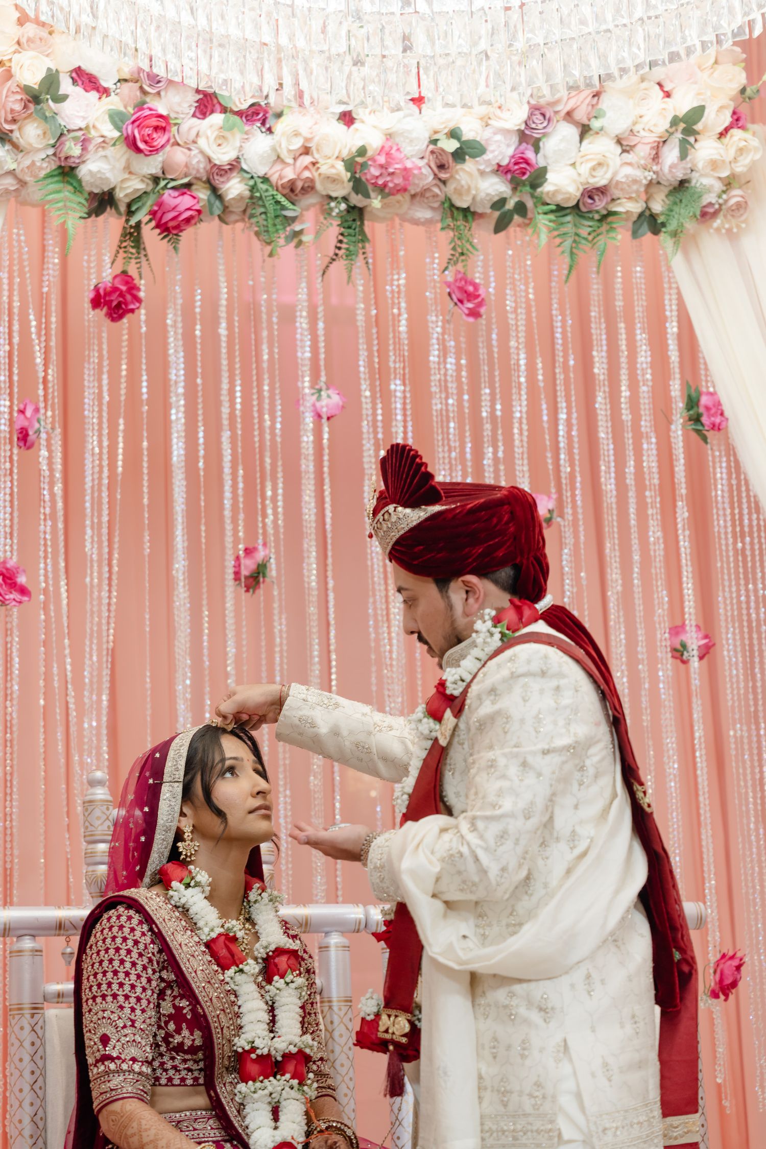 Indian wedding ceremony with pink floral decor and white string curtains creating an elegant backdrop.