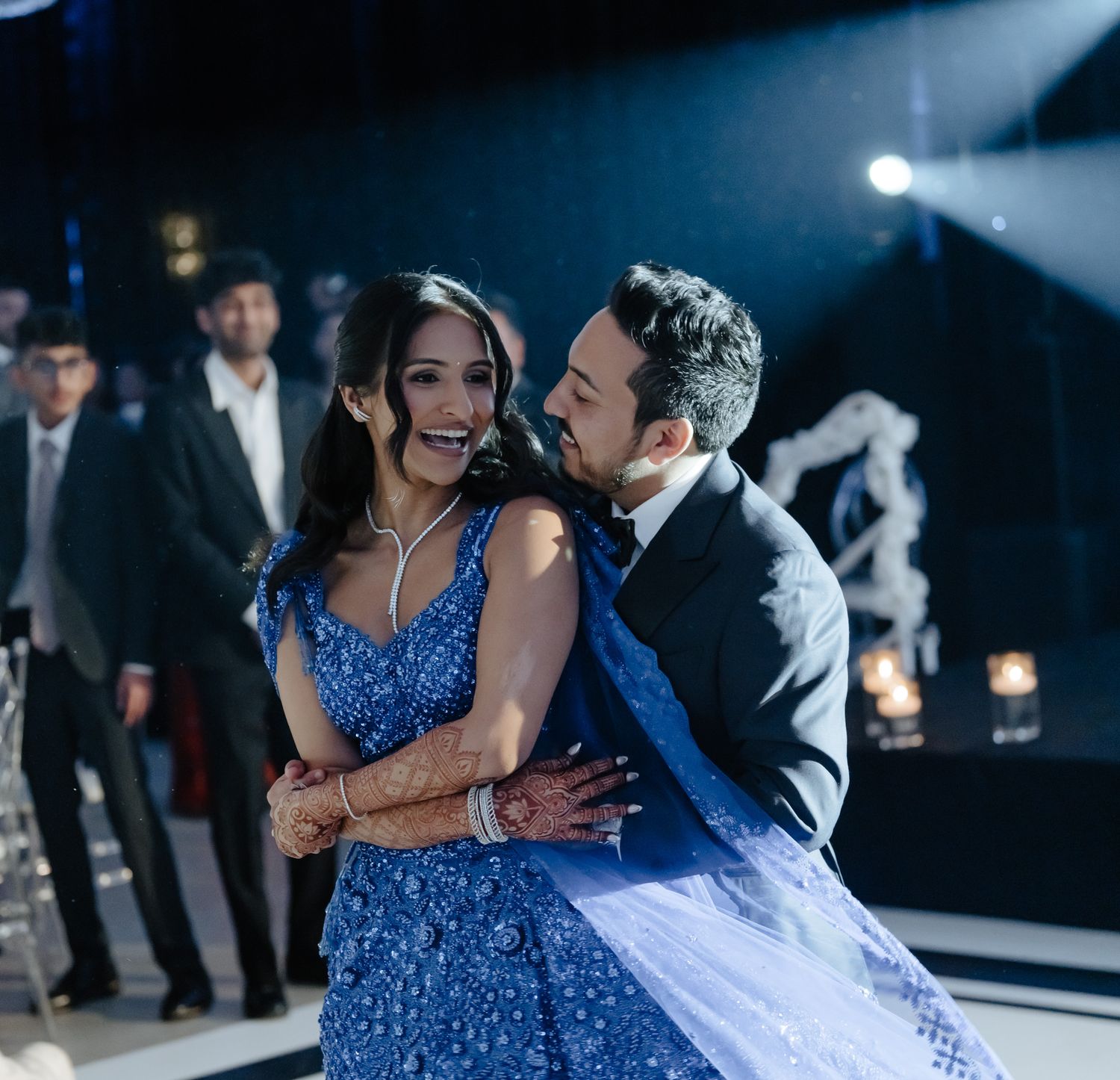 Elegant couple dancing at reception with blue sparkly dress under dramatic lighting.