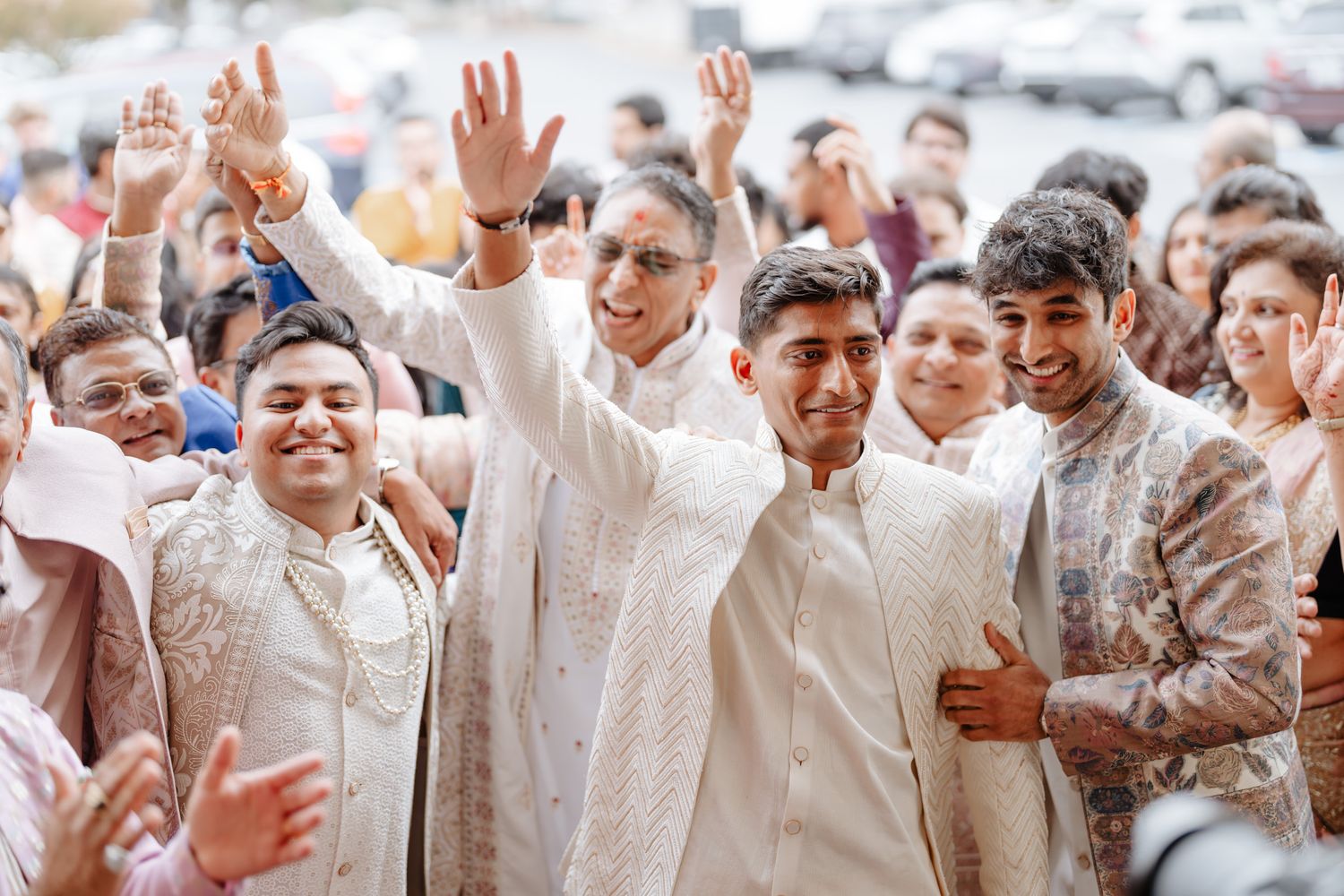 Joyful wedding guests in white attire celebrating with raised hands and excited expressions.