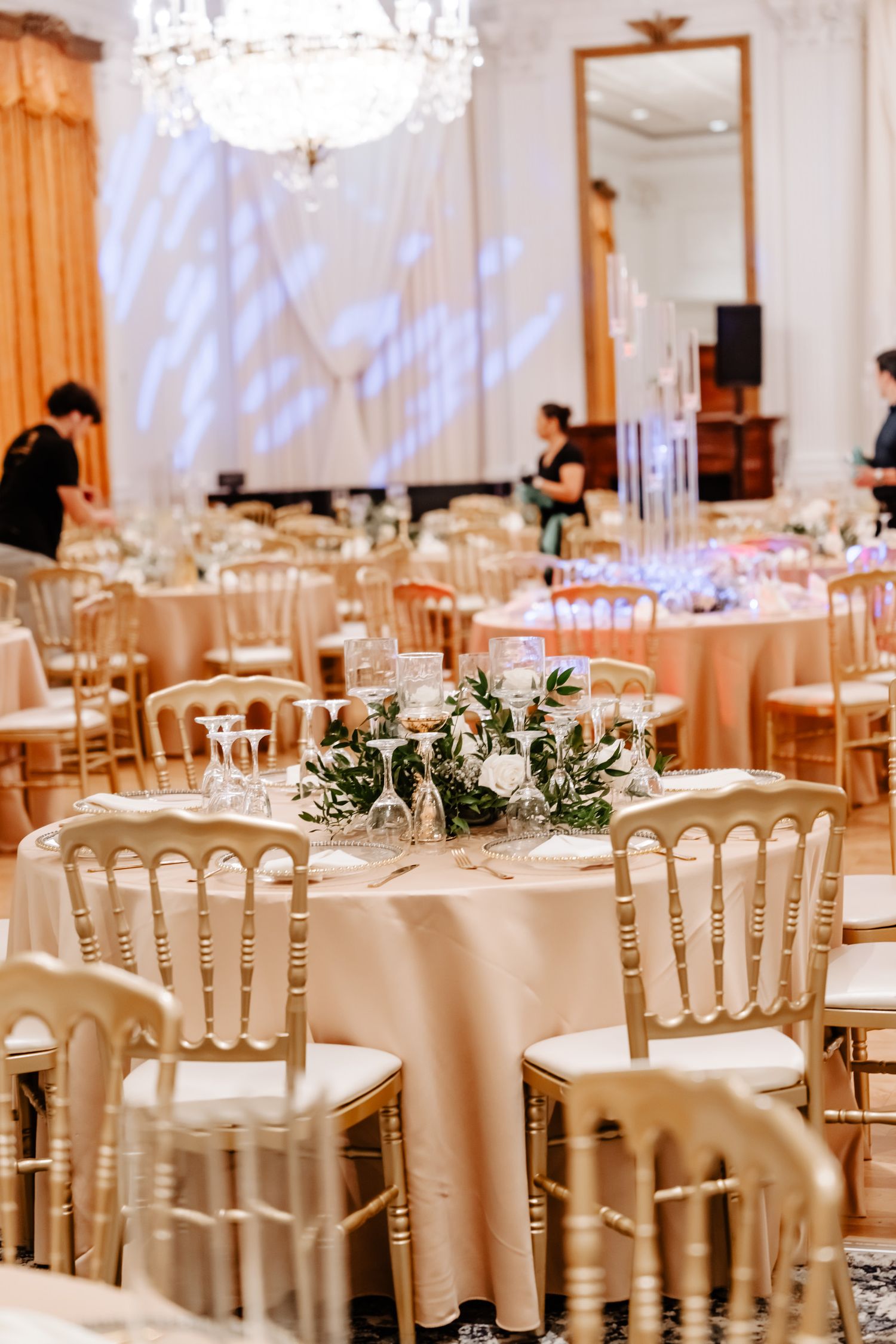 Elegant wedding reception setup with crystal chandelier and gold chiavari chairs.