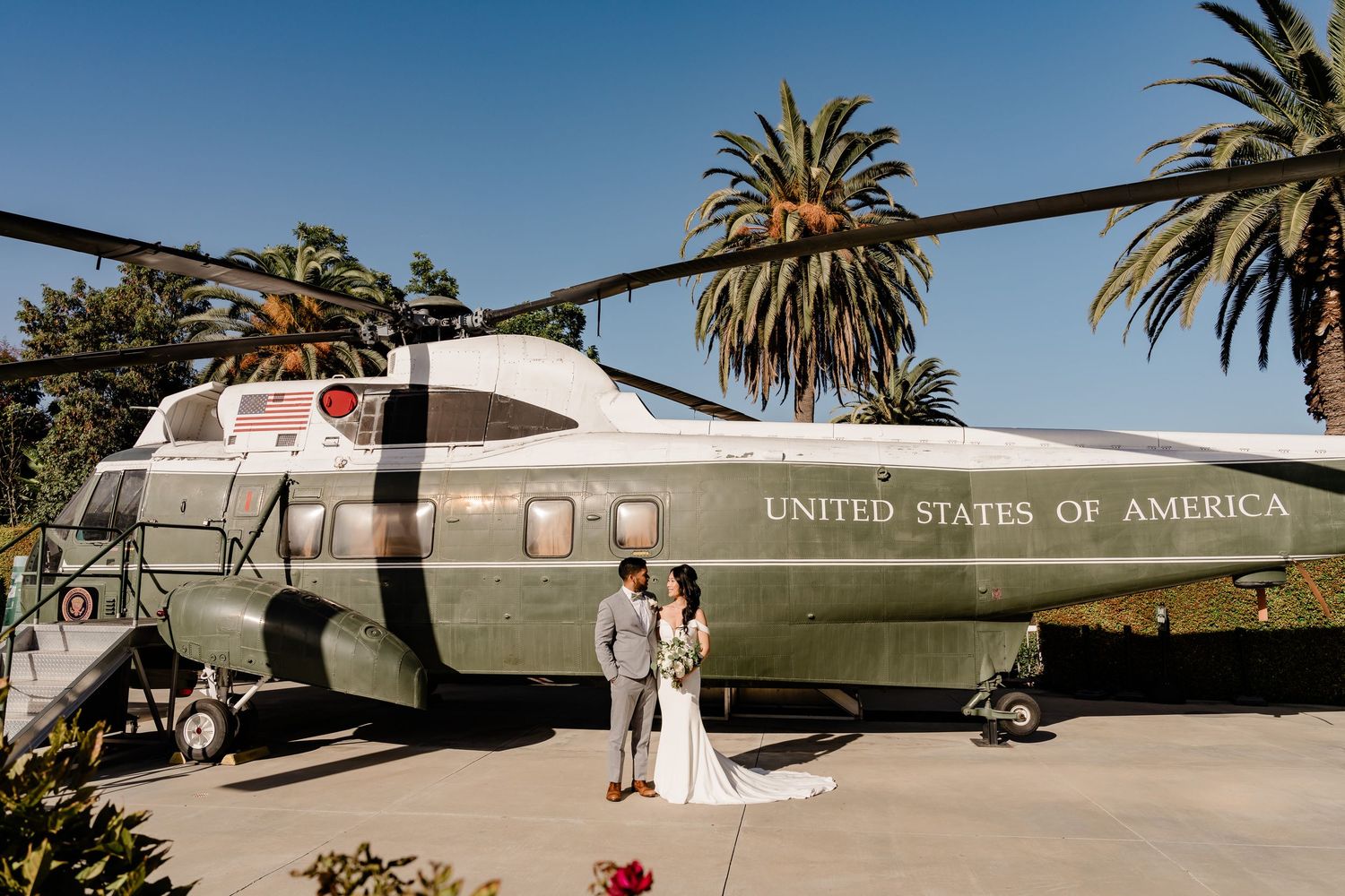 Military aircraft and helicopters on display at an outdoor aviation museum with palm trees in the background.