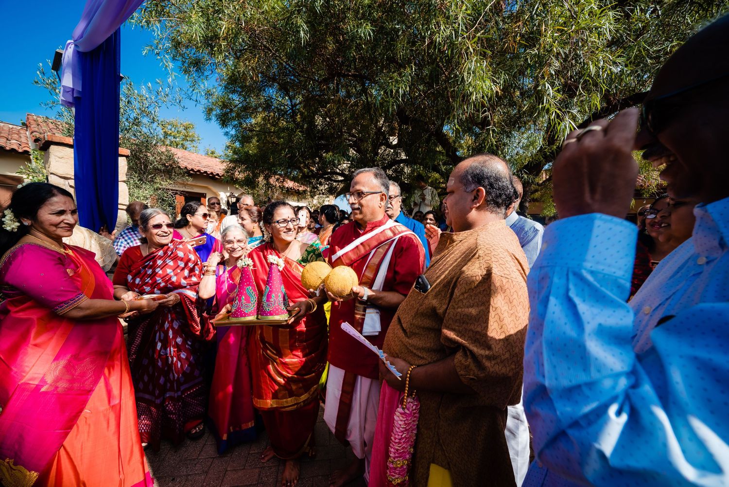 A group of people dance and celebrate together at an outdoor gathering on a sunny day.