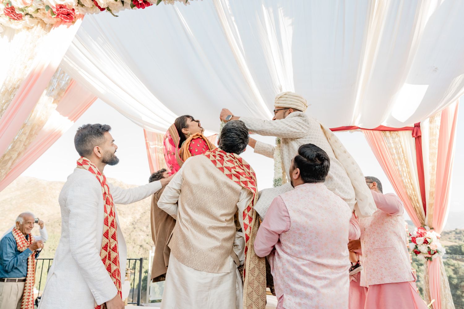 Wedding guests dance and celebrate during a joyful reception under a white and coral draped tent canopy.