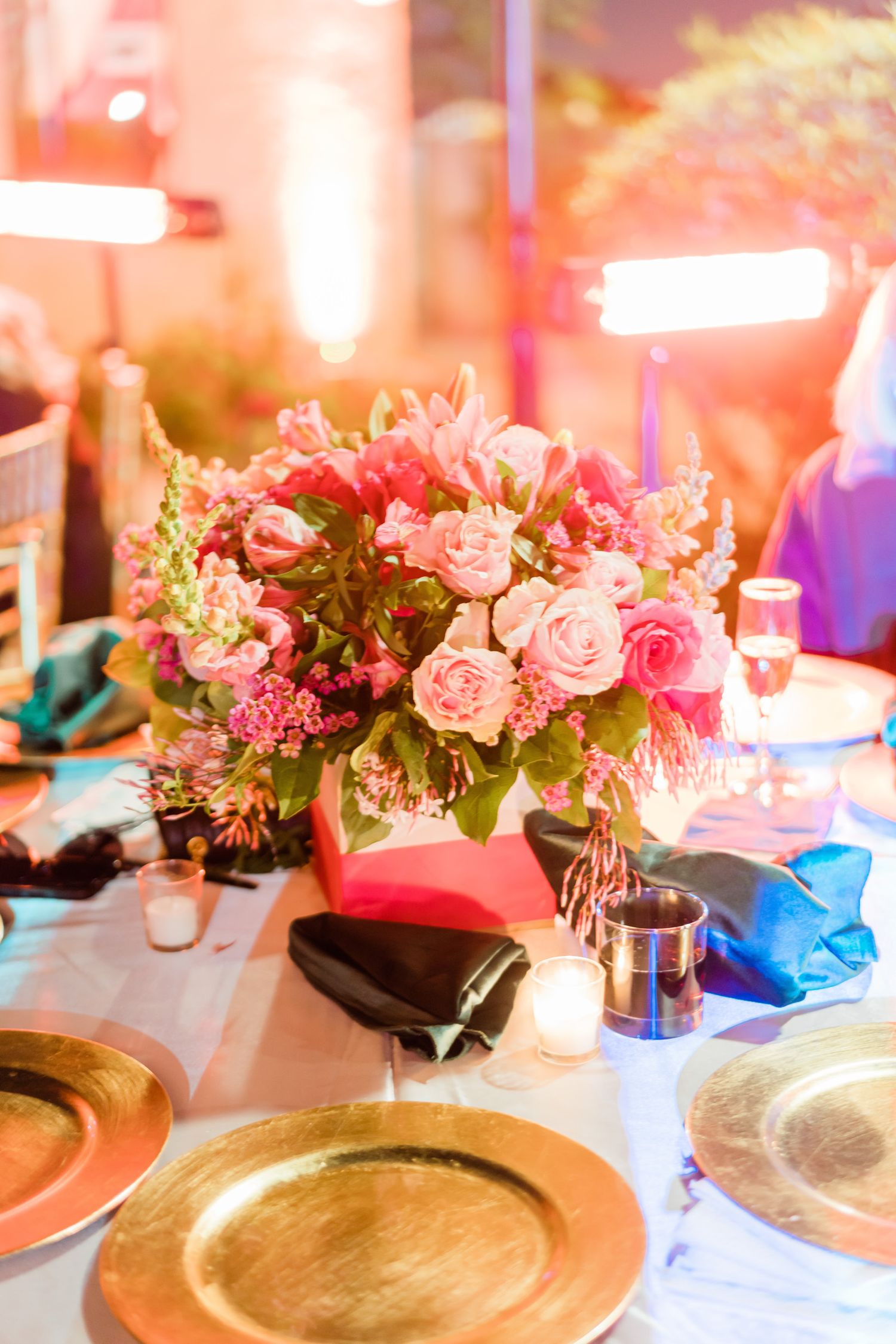 Elegant table setting with pink floral centerpieces and gold charger plates at a formal event reception.