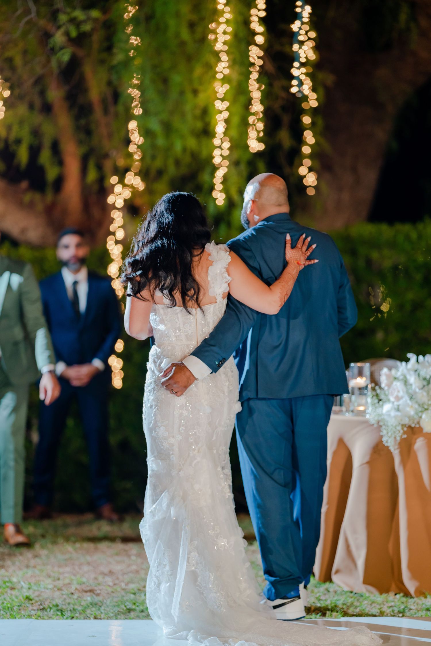 Couple dancing at an outdoor evening wedding reception with string lights and white floral decorations.