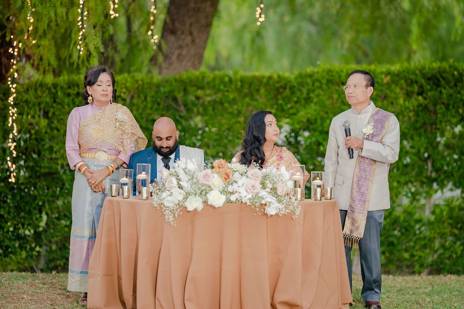 Outdoor wedding celebration with guests mingling around decorated tables and string lights.